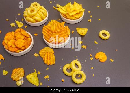 Spuntini salati speziati assortiti. Patatine, anelli, nachos, cracker. In ciotole di ceramica su uno sfondo di pietra Foto Stock