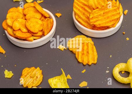 Spuntini salati speziati assortiti. Patatine, nachos, cracker. In ciotole di ceramica su uno sfondo di pietra, primo piano Foto Stock