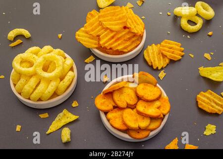 Spuntini salati speziati assortiti. Patatine, anelli, nachos, cracker. In ciotole di ceramica su uno sfondo di pietra Foto Stock