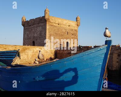 Barca blu con ombra del fotografo sullo sfondo del forte illuminato con luce del mattino. Foto Stock