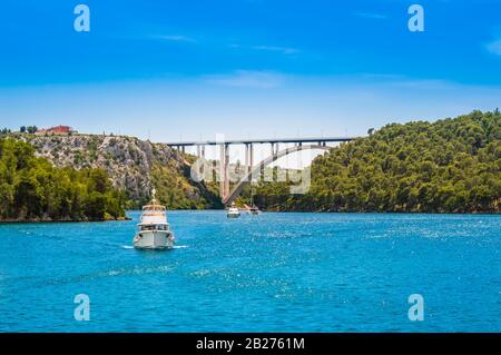 Barche turistiche nel Parco Nazionale di Krka, Croazia. Ponte di Sibenik sul fiume Krka con acqua limpida e cielo blu in una giornata di sole. Foto Stock