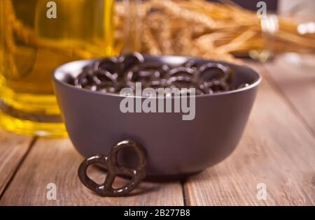 Piccoli pretzel neri in una ciotola con birra di vetro ob sul tavolo di legno Foto Stock