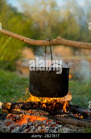Il recipiente nero si sta riscaldando sotto il fuoco. Sfocatura ladscape è in background. Foto Stock