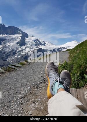 Le gambe si infranagliano in scarpe da ginnastica sullo sfondo delle montagne innevate. La foto simboleggia il "trekking facile" in montagna. Foto Stock