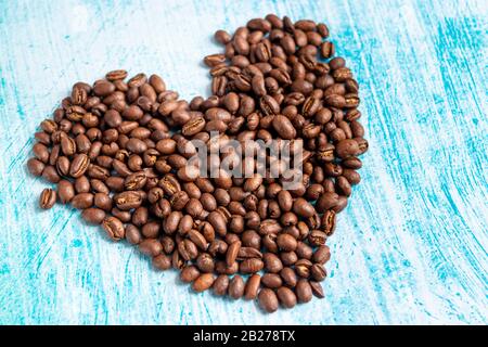 Grani di caffè a forma di cuore su sfondo acquamarina Foto Stock