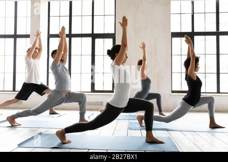 Persone che fanno Warrior uno o Virabhadrasana posa in studio sportivo Foto Stock