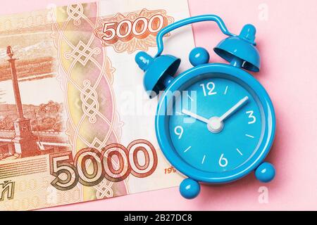 Sveglia e cinquemila rubli russi su sfondo rosa. Concetto di tempo di soldi Foto Stock