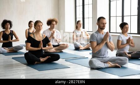 Sette persone diverse piegate mani Namaste simbolo meditando al chiuso Foto Stock
