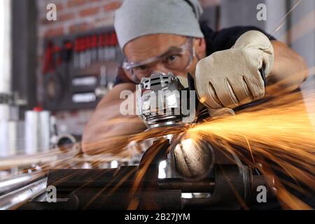 Uomo lavoro in officina di casa garage con smerigliatrice angolare, occhiali di protezione e guanti di costruzione, metallo levigatura fa scintille closeup, fai da te e del concetto di artigianato Foto Stock