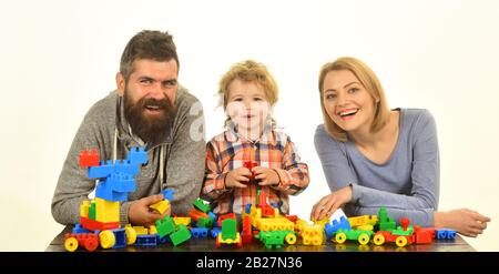 Concetto di infanzia e di gioco. Genitori e bambini in sala giochi. Uomo con barba, donna e ragazzino giocano su sfondo bianco. Famiglia con facce eccitate costruire auto giocattolo da blocchi di costruzione colorati. Foto Stock