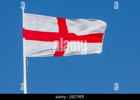 Bandiera dell'Inghilterra di San Giorgio che vola nel vento su un flagpole con cielo blu. Croce rossa su sfondo bianco Foto Stock