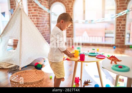 Bella bionda toddler giocando in plastica con cibi e piatti. Piedi intorno un sacco di giocattoli a kindergarten Foto Stock