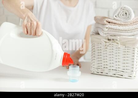 Donna vuole versare il detergente nel tappo sul tavolo, ma il flacone è vuoto, il gel è finito, vicino. Concetto di lavanderia Foto Stock