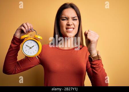 Giovane bella bruna donna che tiene sveglia su sfondo giallo isolato infastidito e frustrato gridando con rabbia, pazzo e urlante con Foto Stock