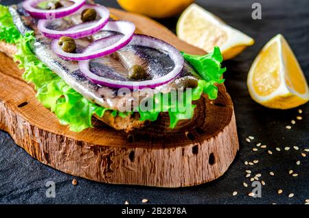 Appetitosi smorrebrod con aringa norvegese, lattuga, cipolla blu, limone e pomodoro si trovano su una tavola di legno Foto Stock