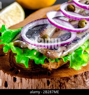 Appetitosi smorrebrod con aringa norvegese, lattuga, cipolla blu, limone e pomodoro si trovano su una tavola di legno Foto Stock