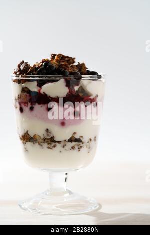 Yogurt Parfait con granola di cacao e mirtilli congelati. Tavolo in legno bianco, luce dura, alta risoluzione Foto Stock