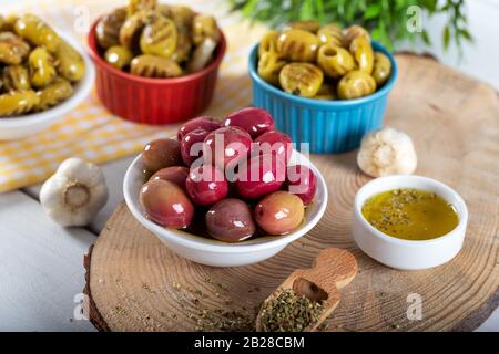 Olive verdi e rosse in ciotola con olio d'oliva e spezie su sfondo di legno Foto Stock