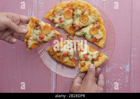 Mani che prendono le fette di pizza dalla piastra, vista dall'alto Foto Stock