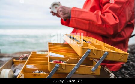 Primo piano di un pescatore che mette su esca con scatola di attrezzatura da pesca. Concetto di pesca e sport. Foto Stock