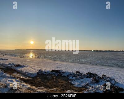 Tramonto sulle rive del fiume Volga ghiacciato. I raggi del sole si riflettono sul ghiaccio. In lontananza puoi vedere la silhouette di un uomo. Copia Foto Stock