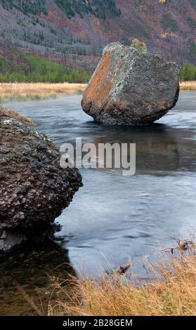 Il grande masso di roccia di colore naturale poggia incommovente nel fiume poco profondo che scorre Foto Stock