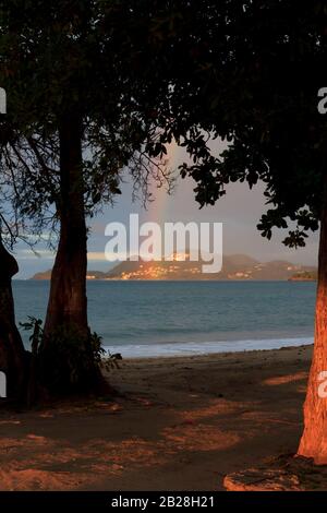 Arcobaleno al tramonto, luce oltre le tenebre, il mare blu scuro tra incorniciato da foglie e tronchi di cedro bianco sulla spiaggia di Vigie Foto Stock