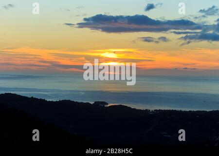 Splendida vista di un tramonto che colorano il cielo arancione e lascia le nuvole viola scuro con le colline in Castries e Rat Island silhouette Foto Stock