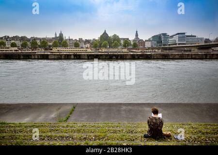 Vista sul fiume Mosa (Maas) che attraversa il centro storico di Maastricht. Seduta donna che legge un libro sulla riverba Foto Stock