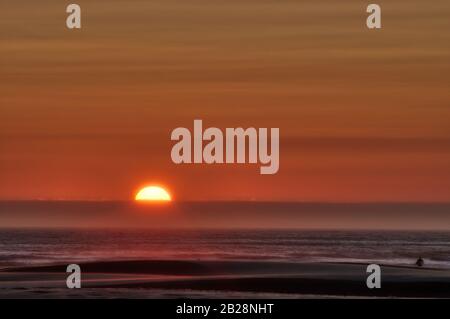 Orange Sun Che Si Trova dietro le nuvole che incorniciano l'orizzonte dell'Oceano Pacifico al largo della costa dell'Oregon Foto Stock