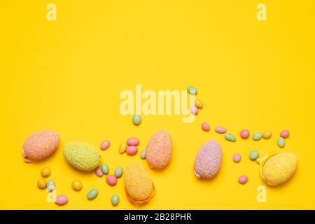 Colore uova di Pasqua e gustosi caramelle colorate fagioli gelatina su uno sfondo giallo con spazio copia, vista dall'alto, piatto lay. Foto orizzontale Foto Stock