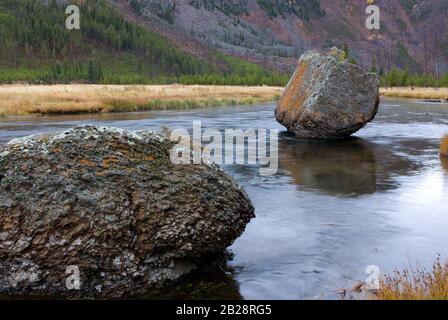 Il grande masso di roccia di colore naturale poggia incommovente nel fiume poco profondo che scorre Foto Stock