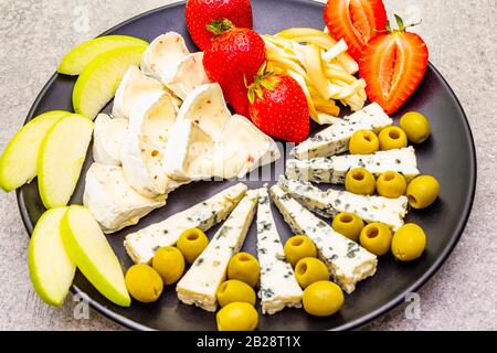 Delizioso piatto di formaggi assortiti. Formaggio bavarese con peperoni jalapeno, formaggio a stampo blu e formaggio a coda di maiale affumicato, frutta e olive. Su un cer Foto Stock