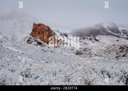 Grande lato di montagna rosso che eruttano fuori dello sfondo nevoso e alta pianura coperta di neve del deserto Foto Stock
