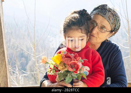 Ritratto di una bambina che tiene un vaso di fiori di fronte al corpo con la sua nonna musulmana senior, stile di vita insieme concetto Foto Stock