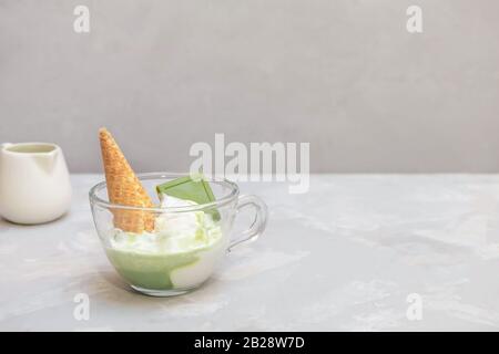 Ricetta Matcha affogato con gelato alla vaniglia e tè verde matcha sano in una tazza di vetro su sfondo grigio, copia spazio Foto Stock