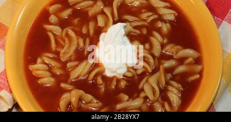 Zuppa tradizionale di pomodoro con panna di saur al centro, con tagliatelle di farina di segale, in piatto giallo / ciotola vista dall'alto primo piano. Foto Stock