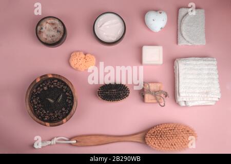 Scrub, lozione, saponi, salvietta di cotone, guanto per la cura del corpo su sfondo rosa. Kit spa eco-compatibile, a disposizione piatta Foto Stock