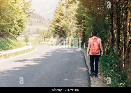 Escursionista femmina camminando per la strada attraverso la campagna, vista posteriore della donna passeggiate lungo la carreggiata su soleggiate giornate estive Foto Stock