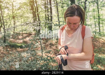 Hiker femmina che controlla il tracker intelligente di idoneità mentre trekking attraverso la foresta Foto Stock
