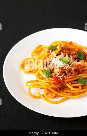 Bucatini fatti in casa tutti Pasta Amatriciana in un piatto bianco su una superficie nera, vista ad angolo basso. Primo piano. Foto Stock