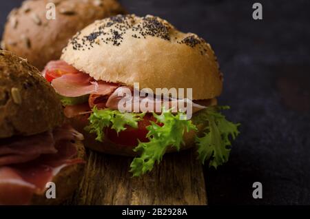 Delizioso hamburger croccante con prosciutto affettato su un tagliere di legno vintage. Foto di cibo scuro ottimo per il menu del bar e i poster. Foto Stock