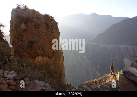 Singola grande roccia di fronte al profondo canyon di Colca (Canon de Colca) in Perù con nebbiose montagne sul Trekkingroute Cabanaconde a Sangalle Oasis Foto Stock