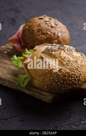 Delizioso hamburger croccante con prosciutto affettato su un tagliere di legno vintage. Foto di cibo scuro ottimo per il menu del bar e i poster. Foto Stock