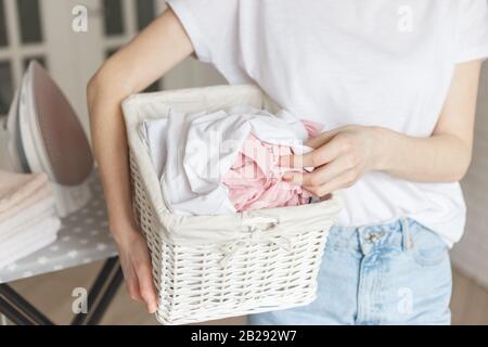 Cesto rustico in vimini con vestiti lavati in mano da donna pronti per stirare Foto Stock
