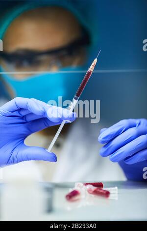 Primo piano di scienziato femminile con le mani gloved che tengono la siringa con il sangue mentre si lavora sulla bioricerca in laboratorio, copia spazio Foto Stock
