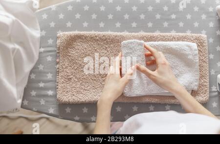Donna che arrotola gli asciugamani puliti che si alzano in piedi all'asse da stiro. Servizio di lavanderia o pulizia di casa concetto Foto Stock