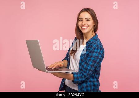 Ritratto di lavoratore freelance sorridente, ragazza felice in casual camicia a scacchi tenendo portatile, utilizzando computer per l'istruzione o il lavoro online, la navigazione intern Foto Stock