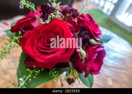 Un piccolo vaso di rose rosse e altri fiori formano un pezzo centrale decorativo. Foto Stock