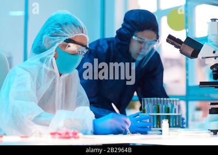 Ritratto della vista laterale di due scienziati che indossano attrezzature a rischio biologico lavorando alla ricerca in laboratorio medico, copia spazio Foto Stock